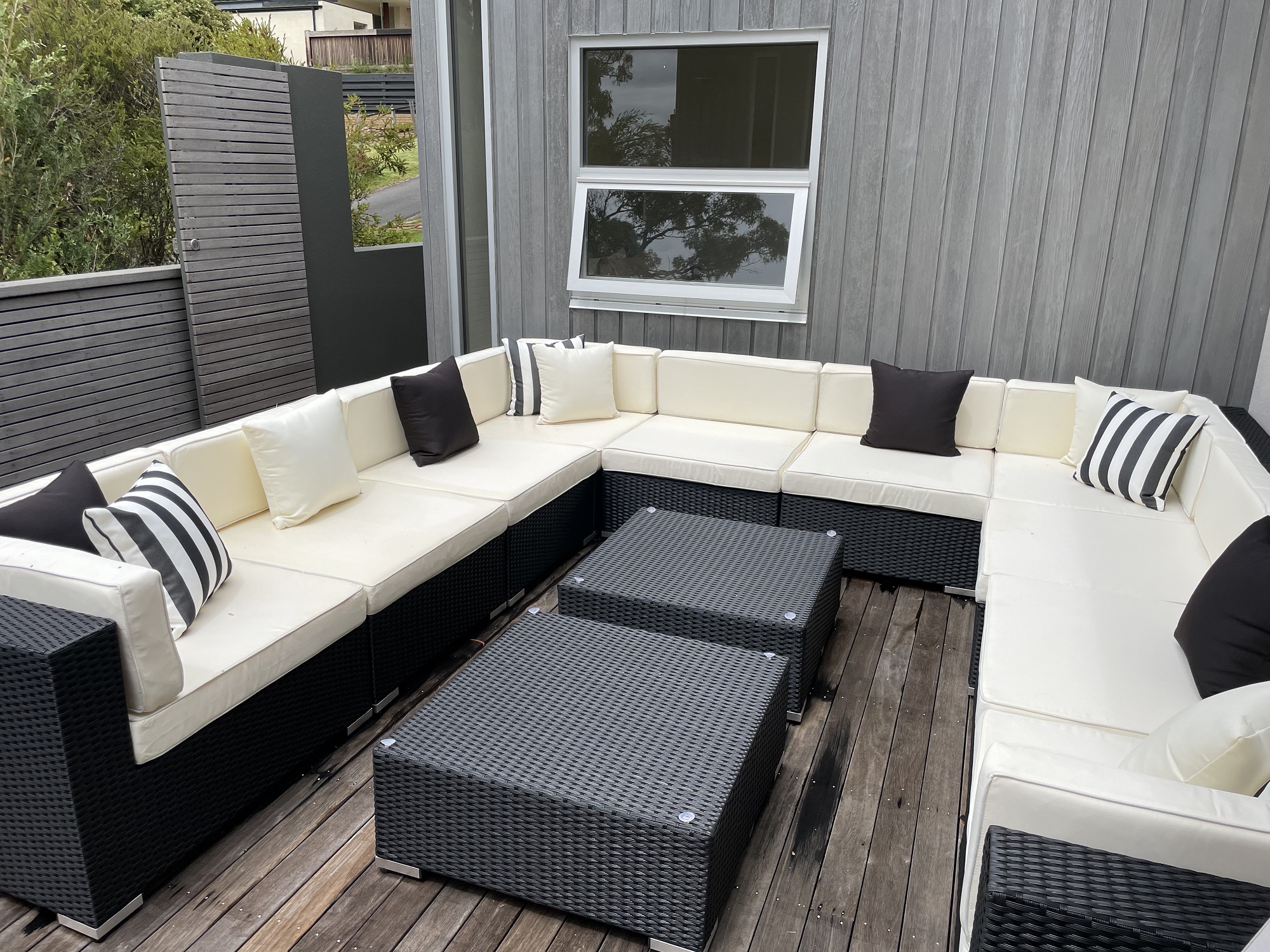 L shape black wicker set with cream cushions on decking