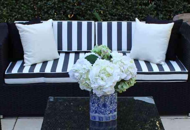 Black wicker sofa with black and white cushions in front of a small black wicker table